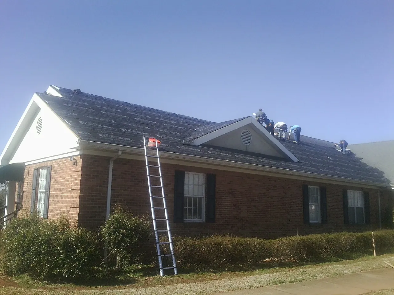 Crew tearing shingles off a brick ranch roof with a ladder set — Emergency Roof Repair work by our crew in Antioch