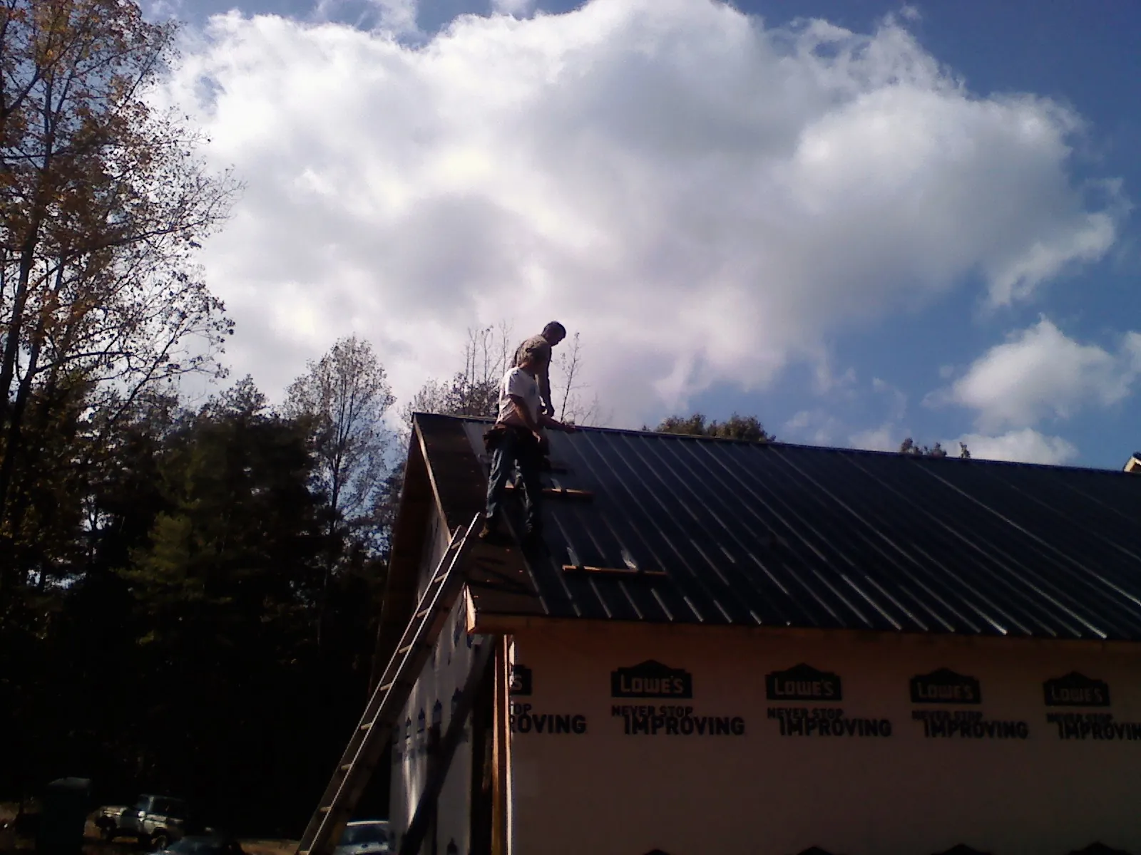 Roofer fastening dark metal panels high against a cloudy sky, from a Roof Inspection job in Antioch