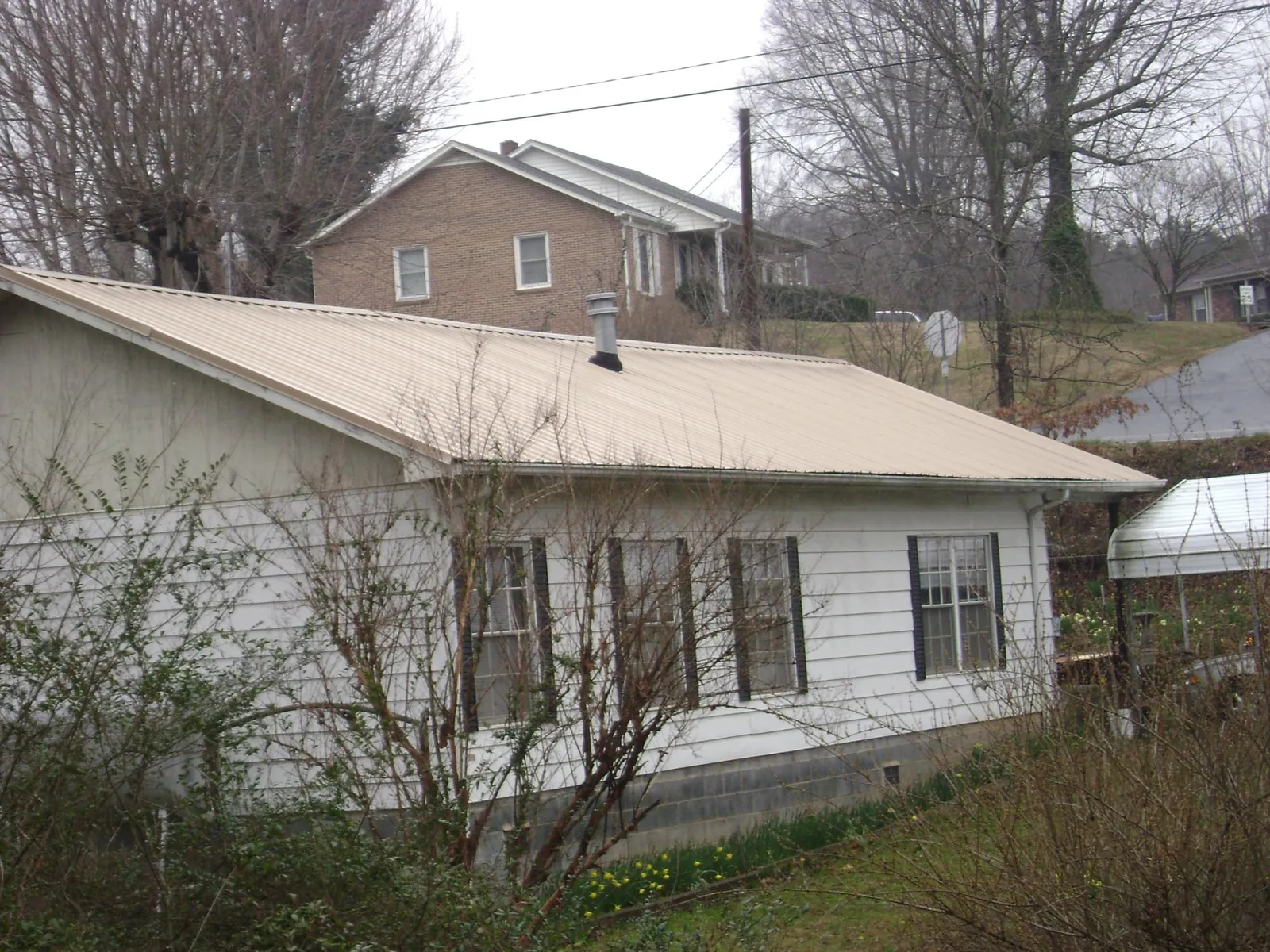 Tan metal roof on a white sided house set into a hillside — Commercial Roofing by Roofing Brothers in Antioch